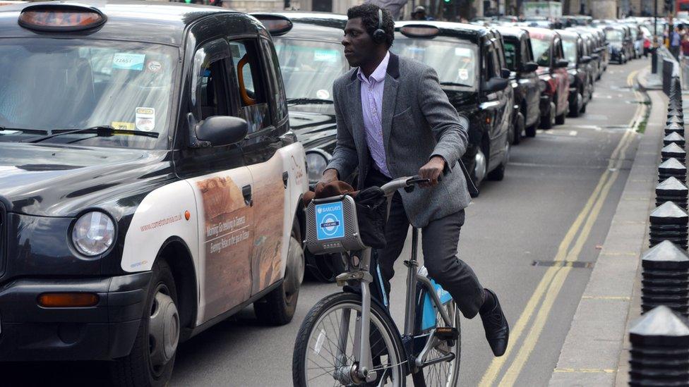 A man on a bike next to a line of taxis