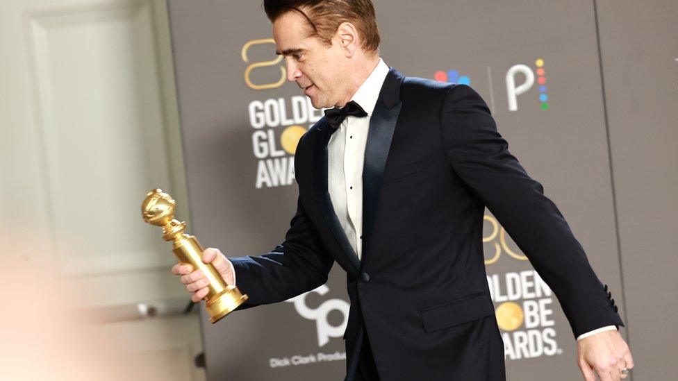 Collin Farrell holds a trophy.