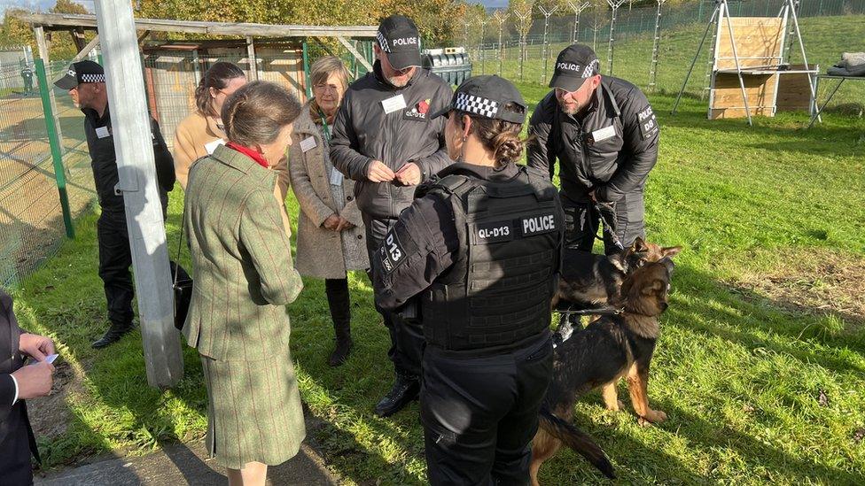 A women in a tweed suit meeting police officers with dogs