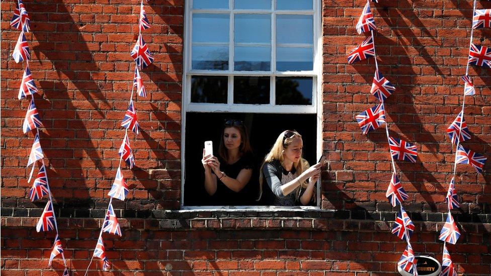 Women take photos on their smartphones as they lean out of the window of a building near Windsor Castle