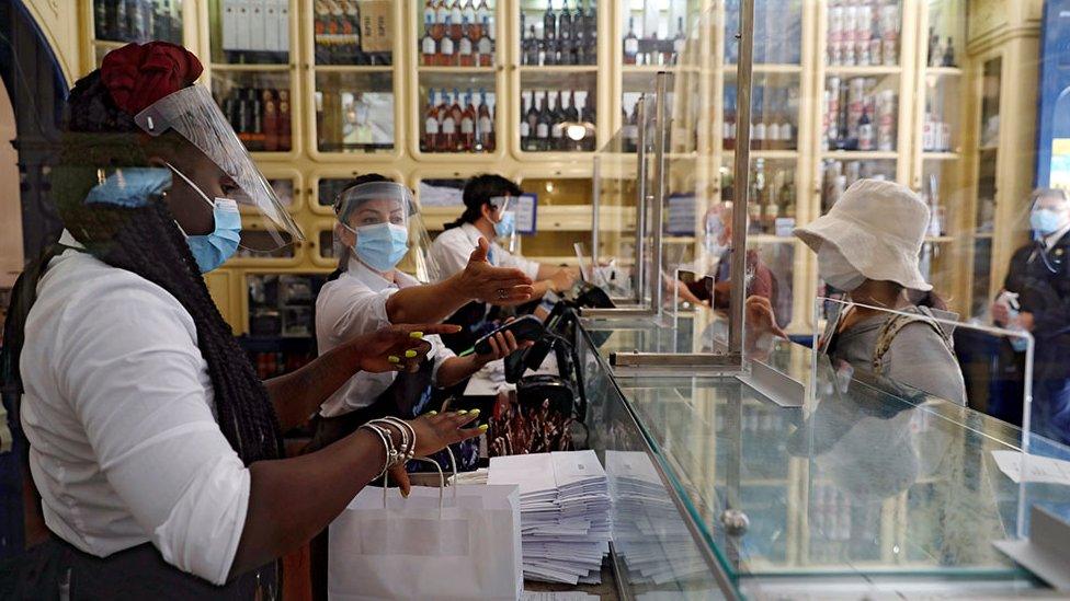 Staff wearing protective masks and face shields serve customers from behind screens at a café in Lisbon