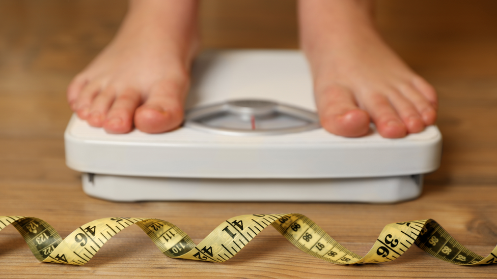 Feet on scales with a tape measure in the foreground