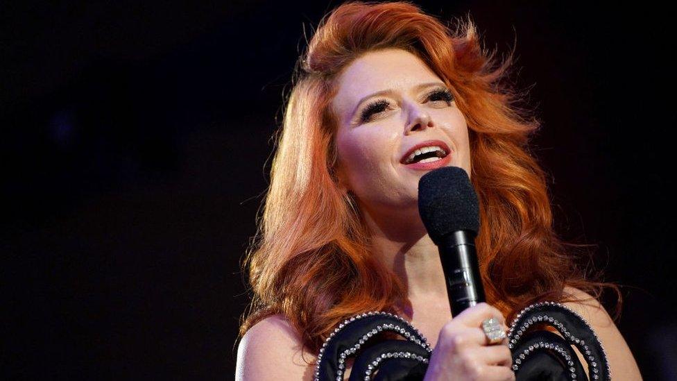 Natasha Lyonne pictured with a microphone in a black dress