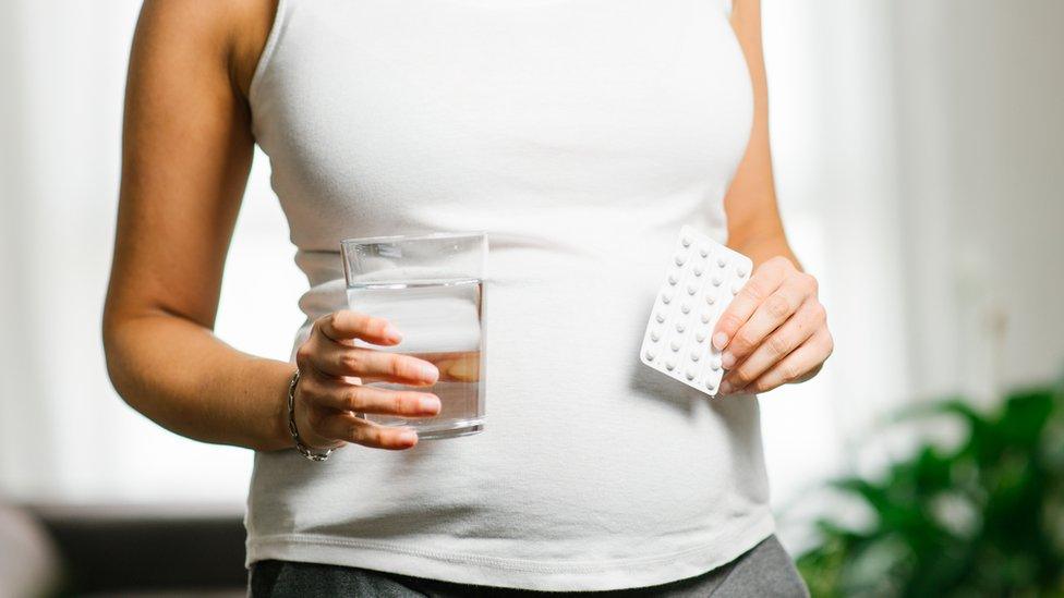 Pregnant woman holding pack of folic acid tablets and a glass of water