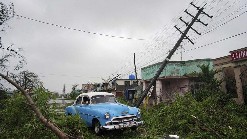 A blue car stuck on a fallen tree and pylon in Cuba.