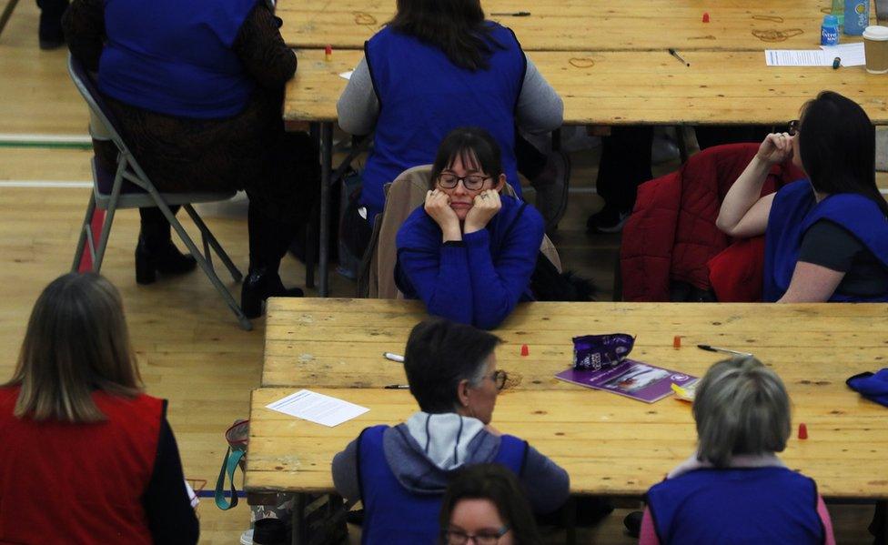 Election count workers sitting at tables waiting for a recount to begin