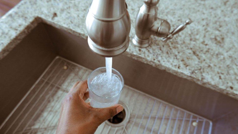 Close-up of a woman filling glass of water from kitchen faucet