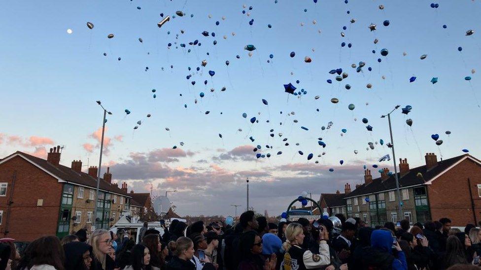 Balloons flying between two lampposts above a crowd of people