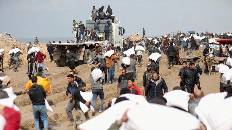 Palestinians carry bags of flour they grabbed from an aid truck near an Israeli checkpoint. February 2024