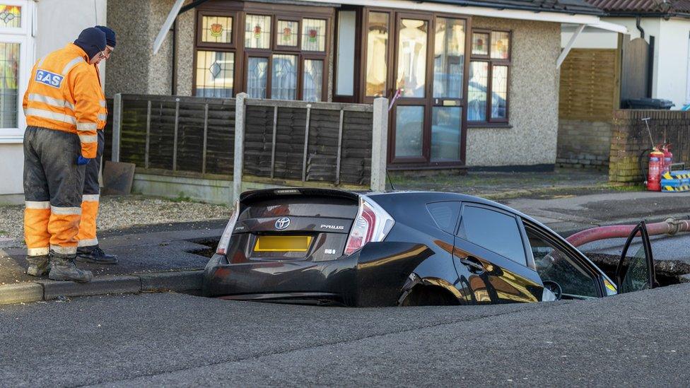 Workers look at the car in the sinkhole