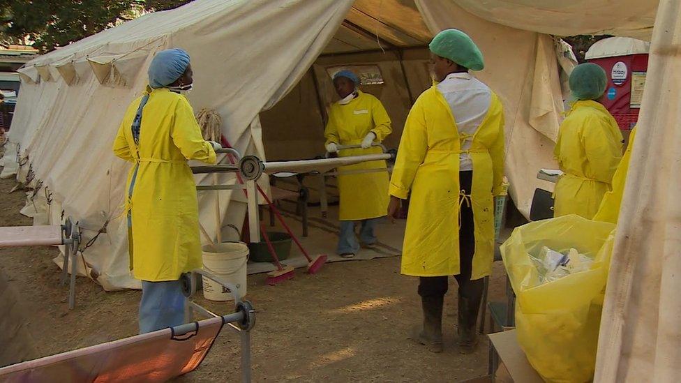 Health workers carry a stretcher into a tent