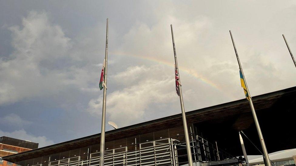 Baneri wedi'u gostwng i hanner ffordd tu allan i adeilad y Senedd ym Mae Caerdydd