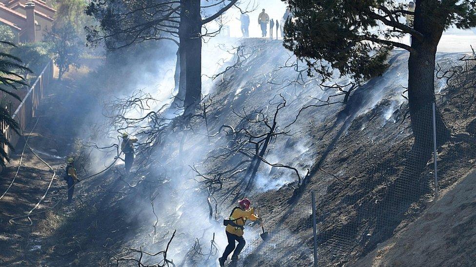 Firefighters work on a charred hillside near homes and the 118 Freeway in Simi Valley, California on October 30, 2019