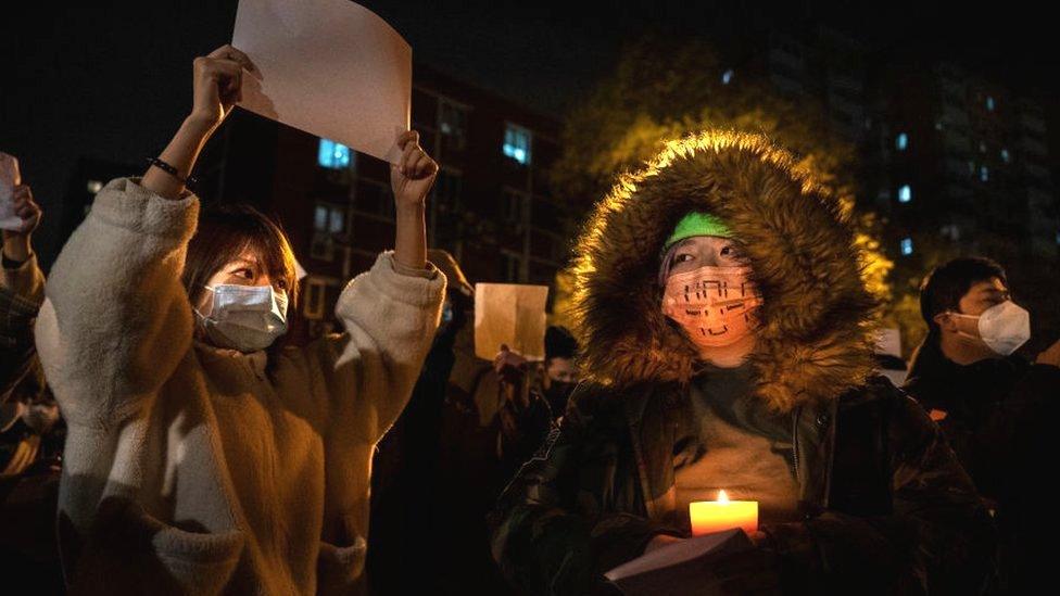 A protester holds a candle as another a white piece of paper against censorship during a protest against Chinas strict zero COVID measures on November 27, 2022 in Beijing, China