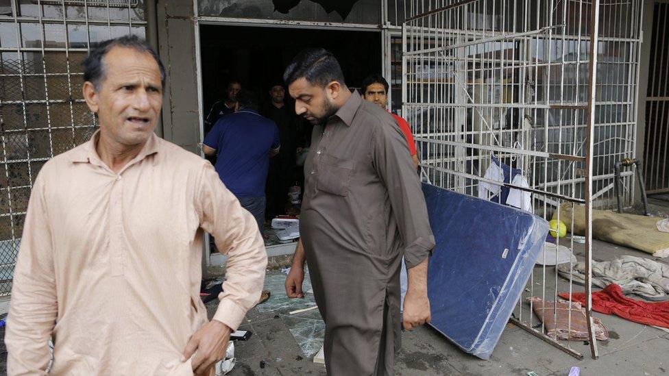 Man stands outside looted shop with broken glass on the floor