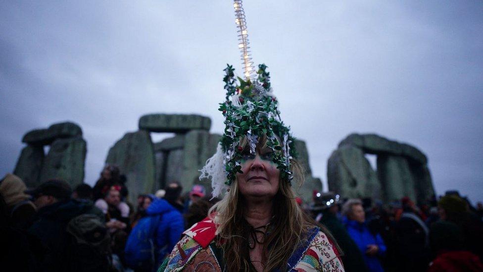 Woman in a light-up headdress in front of Stonehenge