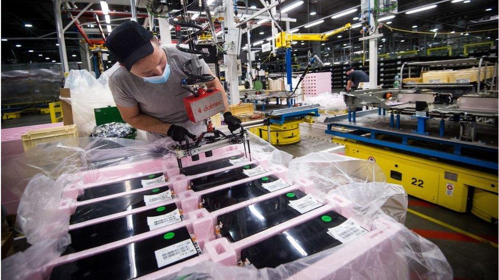 An employee, wearing a protective face mask, assembles a battery-pack for electric cars