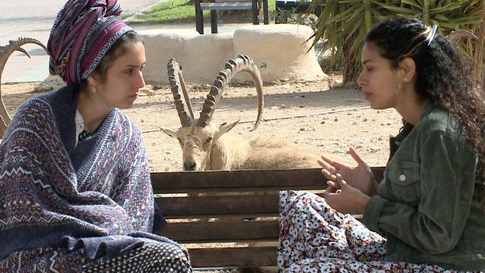 Two women on a bench in front of ibex in Mitzpe Ramon