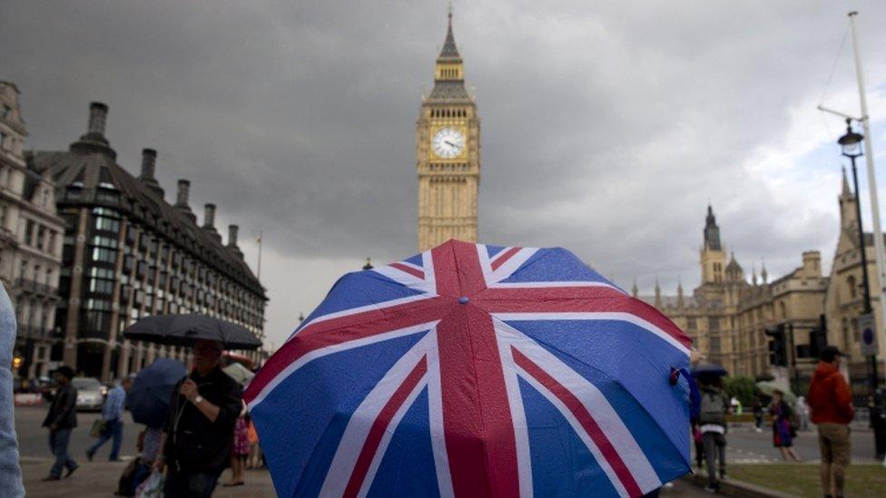 A pedestrian shelters from the rain beneath a Union flag umbrella as they walk near Big Ben