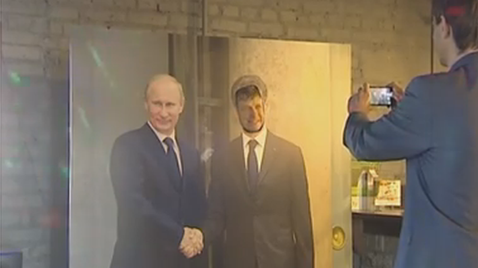 A visitor poses alongside a photo of Putin