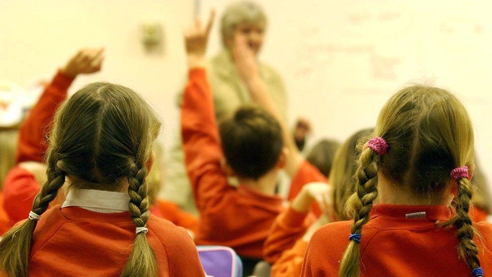 Primary school pupils putting their hands up during a lesson