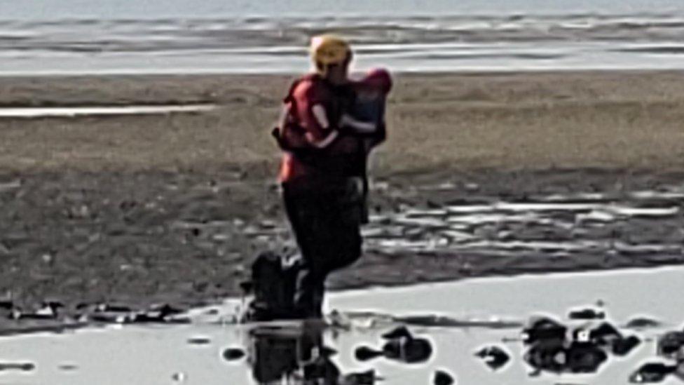 image shows the woman chest-deep in mud while a lifeguard rescues her son