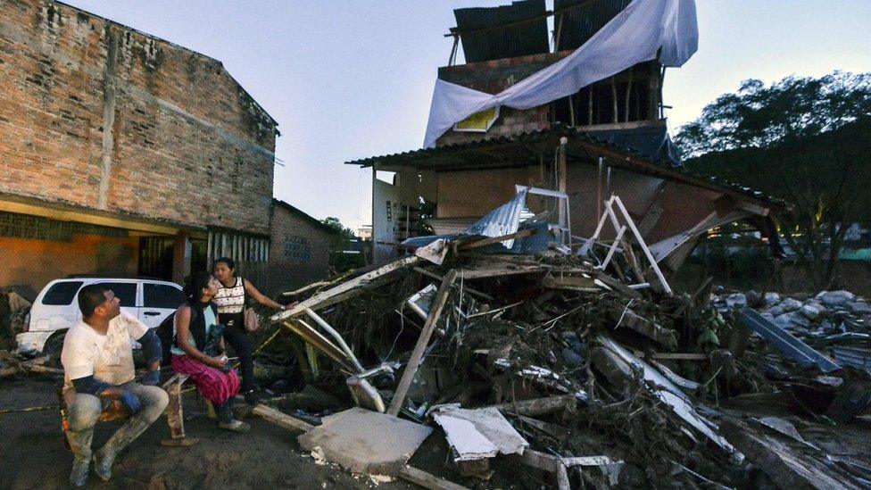 A family wait outside their home damaged by mudslides following heavy rains in Mocoa, Putumayo department, southern Colombia on April 1, 2017