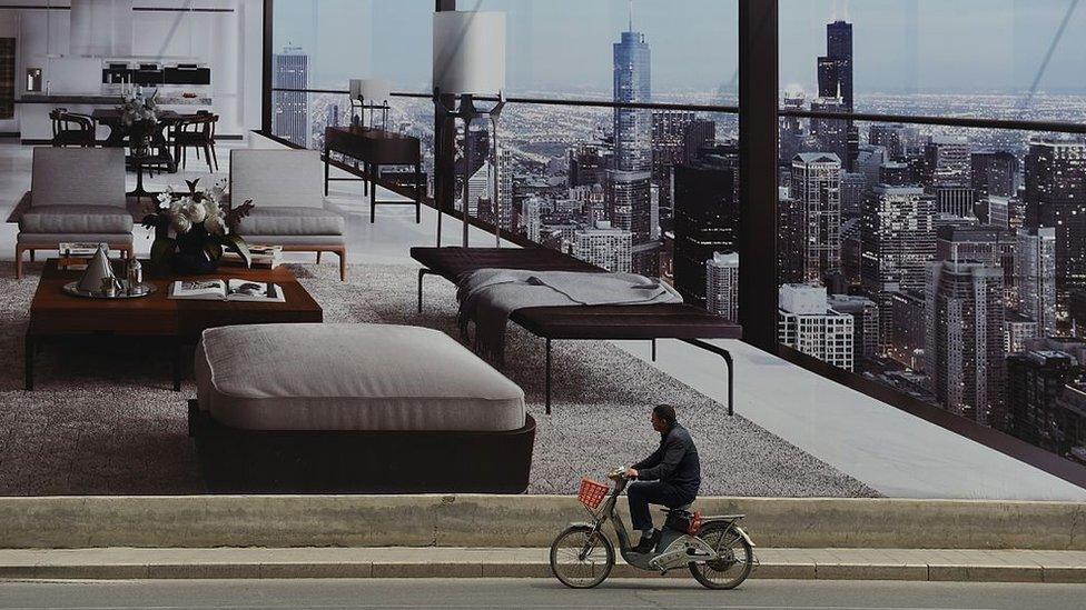 A man cycles past a billboard advertising a new housing complex outside a construction site in Beijing