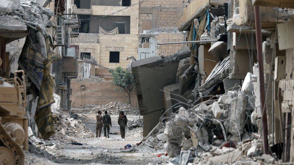 Fighters from Syrian Democratic Forces (SDF) walk together along a damaged street in Raqqa, Syria