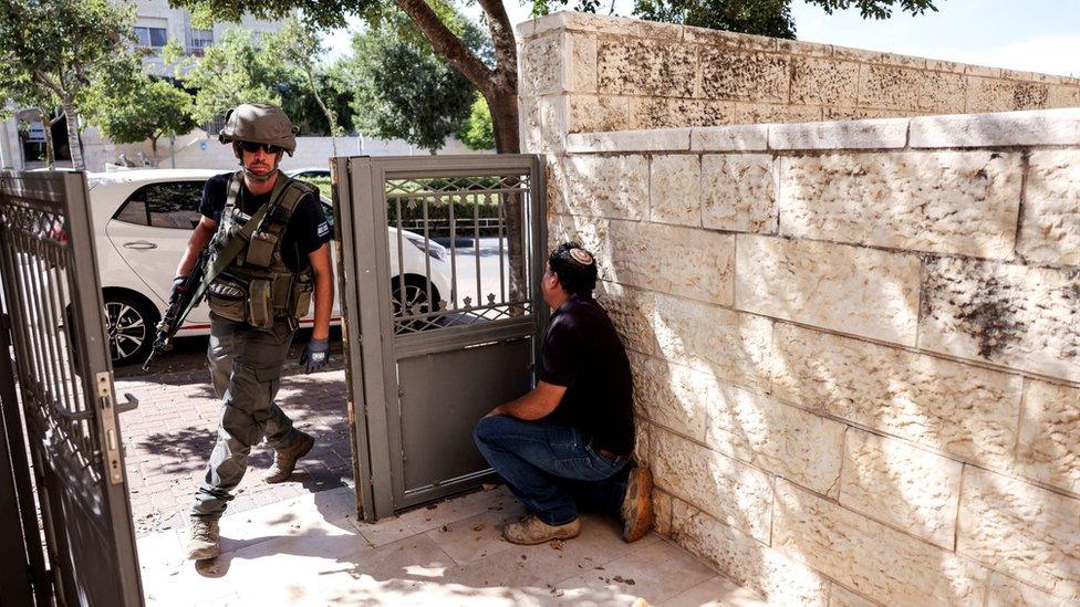 A man takes shelter by a wall as a siren sounds and rockets are launched from the Gaza Strip, in Mevaseret Zion, Israel October 7, 2023.