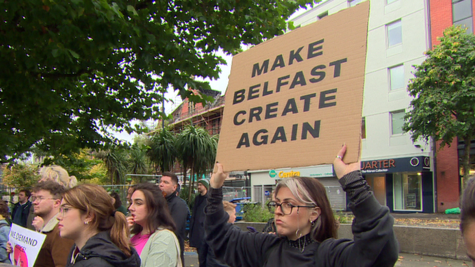 Woman holds up sign saying .Make Belfast Create again'