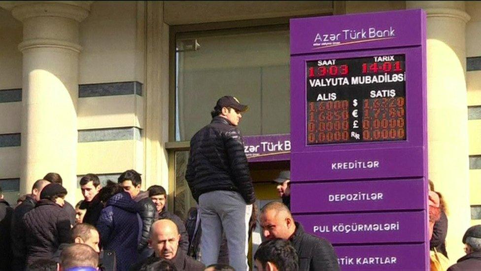 Man standing on wall between queue and bank sign