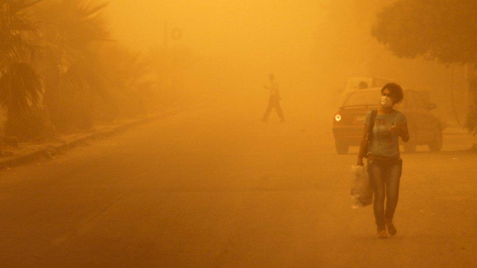 A woman wearing a facemask walks through a sandstorm in Homs, Syria September 7, 2015.