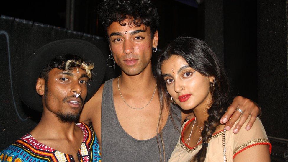 Three South Asian people stand outside a club.