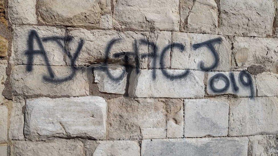 Graffiti daubed in black on the walls of St Oswald's Priory in Gloucester