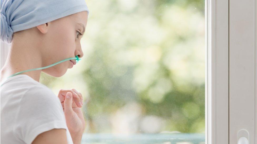 Teenage girl with lung cancer looking through the window in medical centre