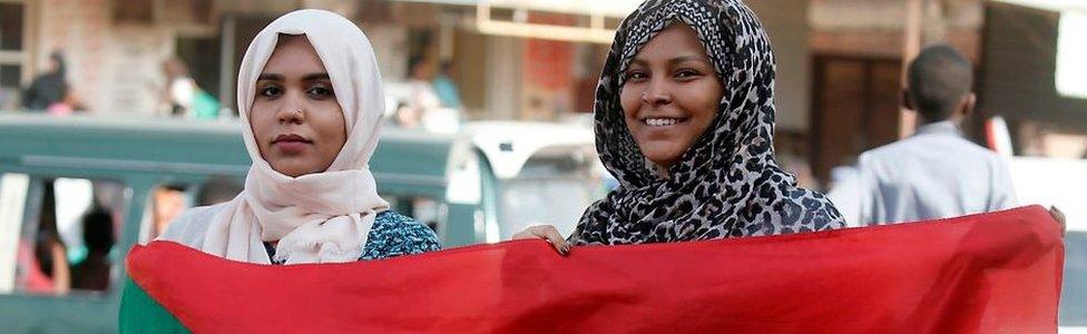 Two women hold a Sudanese flag as Sudanese protesters demonstrate in Khartoum