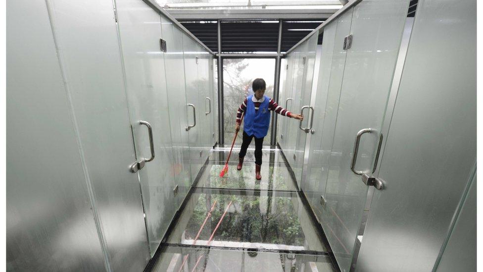 Cleaner walking on glass floor alongside frosted glass cubicles. Changsha, China, 29 September 2016.