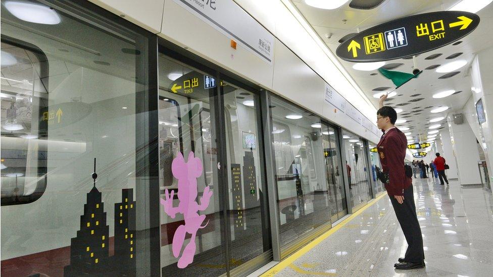 A member of metro staff waves a green flag at the Shanghai Disney Resort metro station, before it opened. Shot on 25 April 2016.