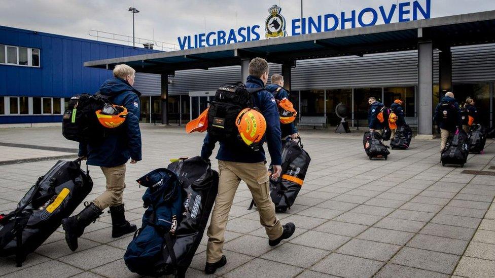 Two Dutch firefighters walk towards airport with bags and helmets