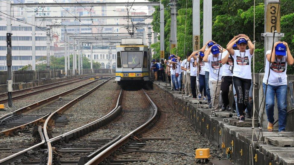 Light Rail Transit (LRT) mock passengers use their hands to cover their heads as they pass through a walkway beside the train tracks during a metrowide simultaneous earthquake drill in metro Manila