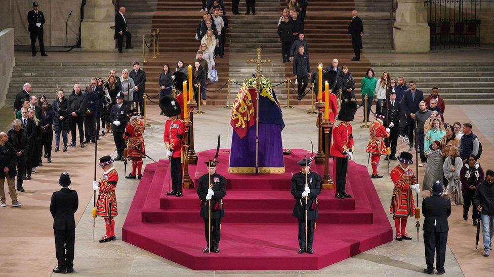 At 4.50am on the day of her funeral the final members of the public pay their respects at the coffin of Queen Elizabeth II, draped in the Royal Standard with the Imperial State Crown and the Sovereign's orb and sceptre, lying in state on the catafalque in Westminster Hall, at the Palace of Westminster, London