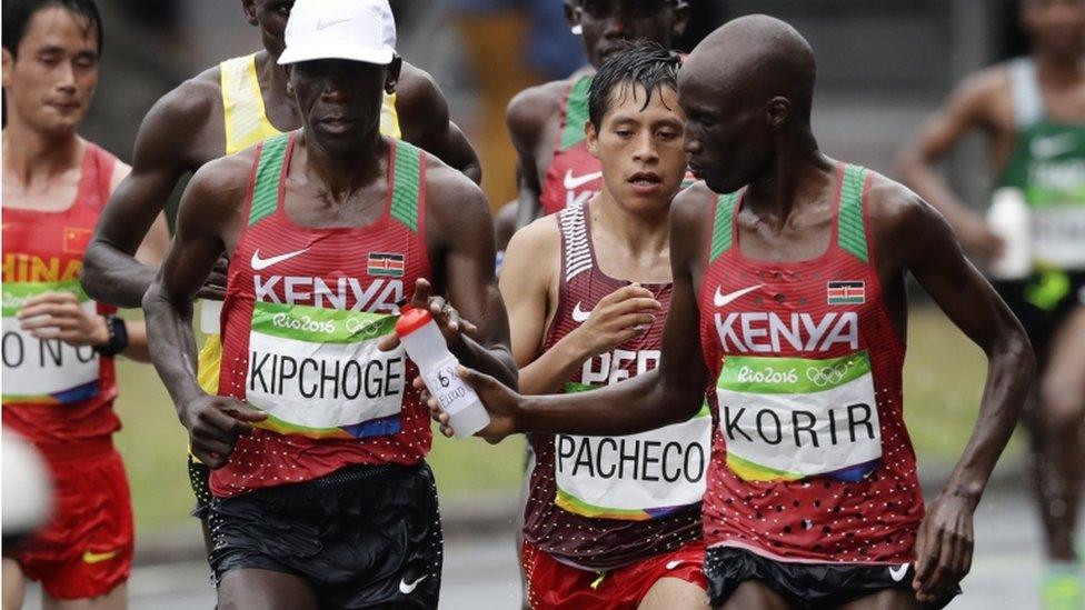 Wesley Korir, of Kenya, right, hands a bottle of water to eventual winner Eliud Kipchoge, also of Kenya, in the men"s marathon at the 2016 Summer Olympics in Rio de Janeiro, Brazil, Sunday, Aug. 21, 2016.