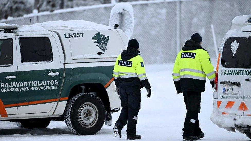 Customs officials walk between Finnish Border Guard vehicles at the Raja-Jooseppi international border crossing station