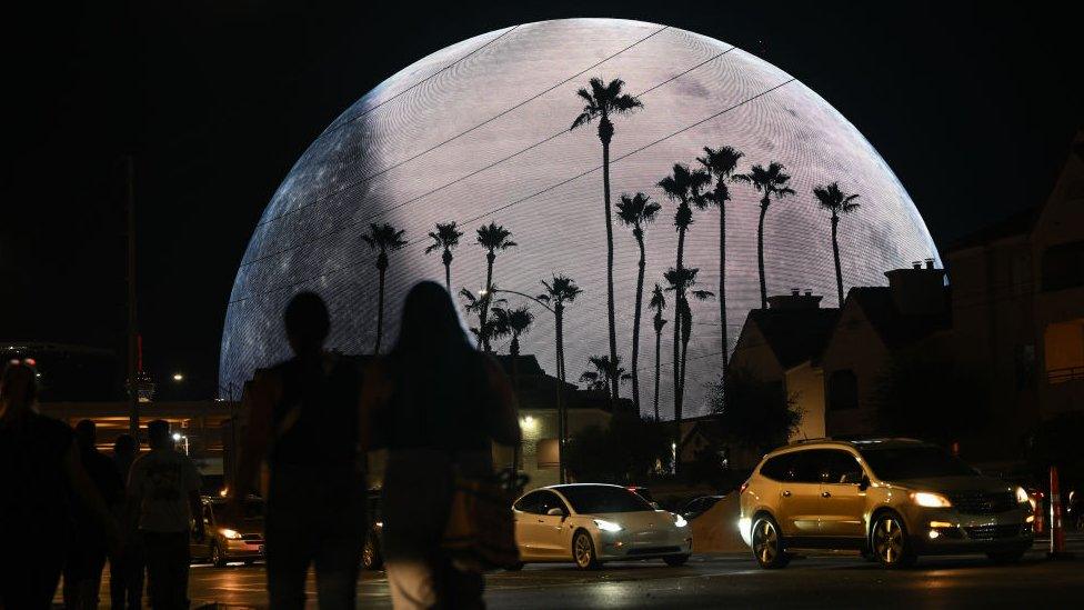 Sphere lit up with palm trees in shadow in front of it.