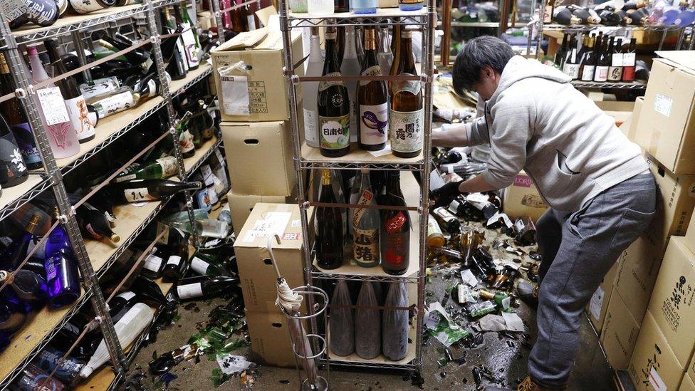 Store owner cleaning up smashed bottles in Fukushima liquor shop