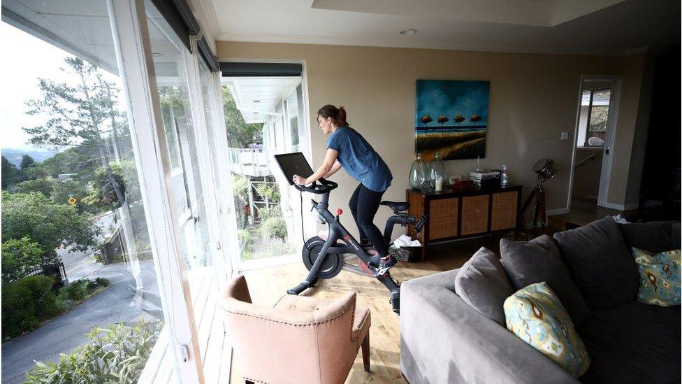 A woman riding a peloton bike at home in the living room