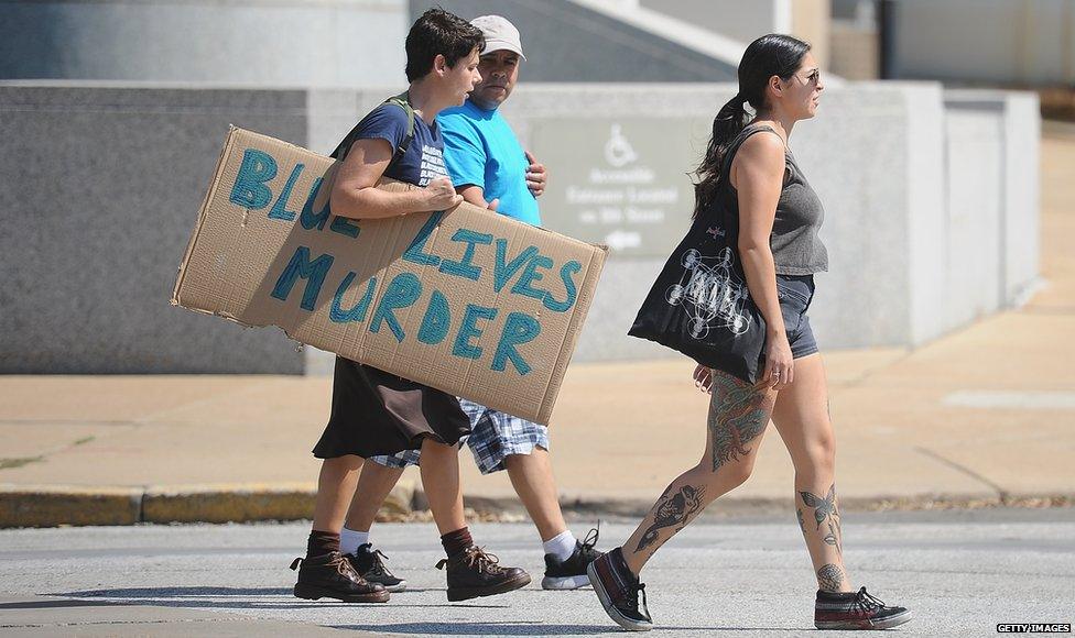 A woman holding a banner that reads 'Blue Lives Murder'