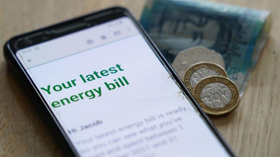 Mobile phone showing energy bill next to coins and a £5 note