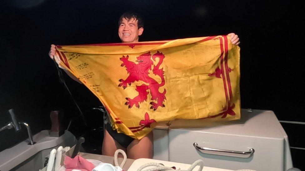 Andy Donaldson holds a Scottish Lion Rampart flag aloft on a boat